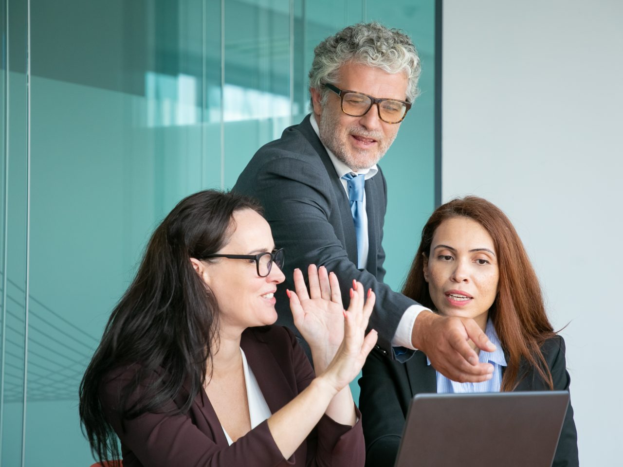 Business team watching and discussing presentation on laptop, male executive pointing at display, while female managers explaining details. Medium shot. Communication and teamwork concept